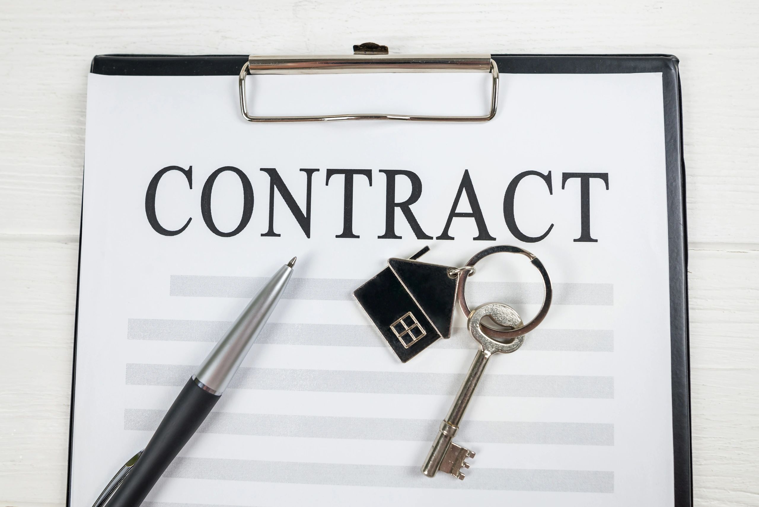 Top view of blank house lease or purchase agreement form with clipboard and key on white table.